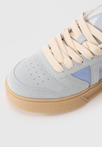 Lyseblå semsket sneakers med kremfargede snørebånd, perforert tåboks og teksturert gummisåle. Har en blå aksent på siden.