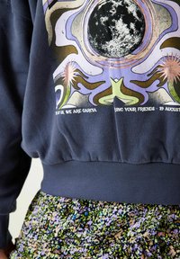 Mörkblå sweatshirt med en f ärgglad grafisk design med himmelska motiv och text. Ribbad mudd och nederkant, kombinerad med en blommönstrad kjol.