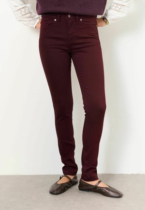 Person wearing fitted burgundy pants, white long-sleeve blouse with lace details, and dark brown flat shoes with ankle straps.
