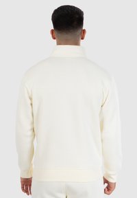 Witte pullover sweatshirt met hoge kraag, gemaakt van gladde stof. Ribgebreide manchetten en zoom verbeteren de pasvorm. Eenvoudig, strak ontwerp zonder patronen.