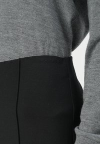 Maglione grigio a maglia abbinato a pantaloni elasticizzati neri a vita alta con logo Calvin Klein sulla cintura. Evidente contrasto di tessuti testurizzati.
