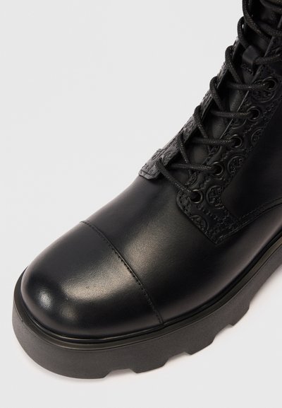 Botín de cuero negro con punta redondeada, panel lateral texturizado y suela de goma gruesa con un patrón de tacos. Incluye cordones y detalles de costura.