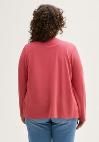 Langarm-Cardigan aus hellrosa strukturiertem Stoff, mit geradem Schnitt und lockerer Passform, kombiniert mit blauen Jeans.