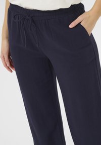 Pantaloni blu navy, morbidamente aderenti e larghi, realizzati in tessuto soffice, con una vita elasticizzata dotata di cordino e tasche laterali.
