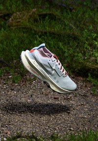 Scarpa da corsa grigia chiara con tomaia in mesh testurizzato, accenti rosa e suola maculata; presenta ammortizzazione e un marchio ben visibile.