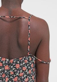 Robe d'été fleurie avec un fond noir, ornée de fleurs roses et vertes. Fines bretelles et corsage ajusté menant à une jupe fluide.
