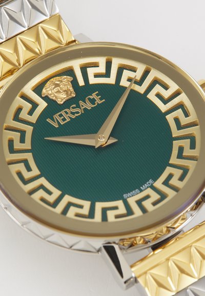 Montre en or et en argent avec un cadran vert, arborant un motif en clé grecque, le logo Versace, et une surface texturée. Étiquette Swiss Made incluse.