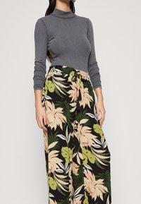 Col roulé gris côtelé associé à un pantalon large noir à motif floral avec des feuilles vertes et roses, doté d'une taille à cordon.