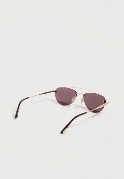 Sleek sunglasses with thin gold metal frame, dark purple tinted lenses, and black curved temple tips, resting on a white surface.
