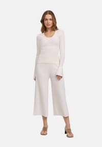 Ivory ribbelgebreide top met lange mouwen en een ronde halslijn, in combinatie met bijpassende flared broek; zachte textuur, elegante silhouet.
