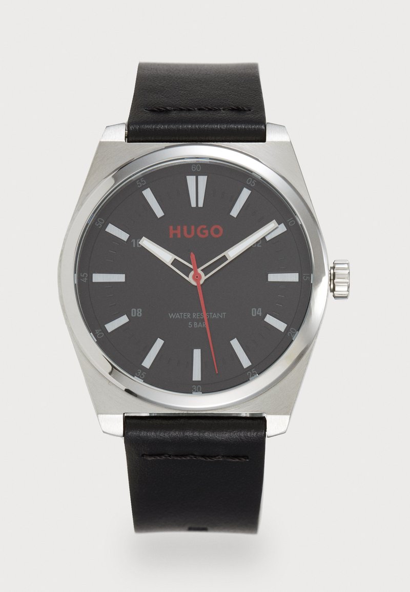 Reloj Hugo con correa de cuero negra, caja de acero inoxidable plateada, dial negro, marcadores de hora blancos y acentos rojos, resistente al agua hasta 5 bares.