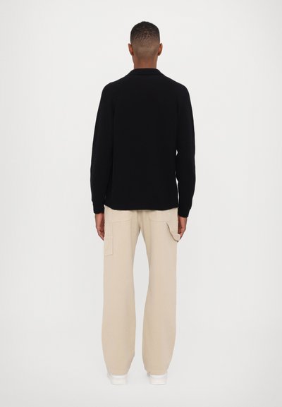 Pull en maille noir avec col, associé à un pantalon cargo beige ample. Design minimaliste, sans motifs ni embellissements visibles.