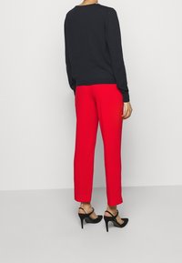 Un pull noir à manches longues, un pantalon rouge ajusté et des sandales à talons noires. Tissu lisse, design ajusté, pantalons de longueur cheville et chaussures à dos ouvert.