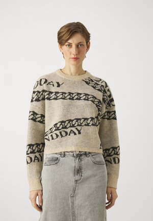 Knit sweater in beige with black chain pattern and text. Ribbed crew neckline and cuffs, cropped design, soft texture. Paired with a gray denim skirt.