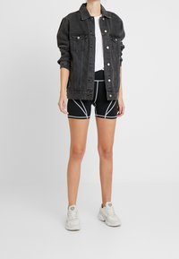 Czarna dżinsowa kurtka z guzikami, biała koszulka, czarne szorty z białymi akcentami i białe buty sportowe. Prosty, casualowy zestaw.