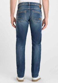 Jeans de mezclilla azul oscuro con pierna ajustada, que presentan dos bolsillos traseros y una etiqueta de cuero en la cinturilla, mostrados desde la parte de atrás.