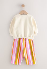 Sweat-shirt en coton blanc cassé avec col rond, associé à un short en coton rayé vibrant rose, orange, jaune et bleu.