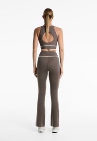 Braunes Sportoutfit bestehend aus einem ärmellosen Oberteil mit ausgeschnittenem Rücken und hoch taillierten, ausgestellten Leggings. Der Bund hat einen kontrastierenden weißen Streifen.