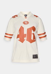 Krémový NFL dres s oranžovými akcenty, na přední straně s číslem 46 a logem. Krátké rukávy s dvěma bílými pruhy.