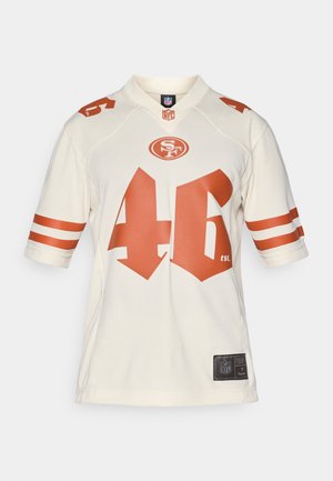 Krémový NFL dres s oranžovými akcenty, na přední straně s číslem 46 a logem. Krátké rukávy s dvěma bílými pruhy.