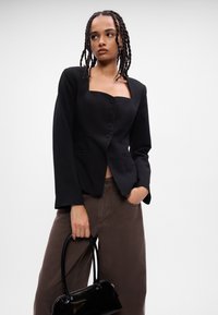 Melna īsā žakete ar kvadrātu veida kakla izgriezumu un piecām pogām. Garas piedurknes, strukturēta piegriezuma, apvienota ar brūnām platām biksēm un melnu somu.