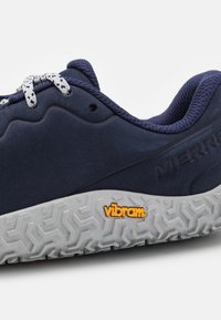 Zapato azul marino con superficie texturizada, que presenta una suela blanca con patrón y cordones grises. Logo de Vibram destacado en naranja.