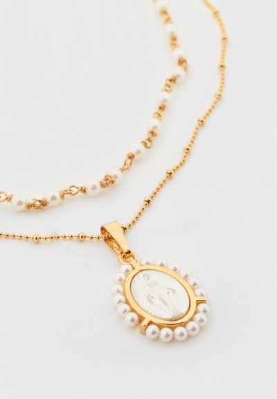 Collier pendentif en or avec de petites perles entourant une figure religieuse, associé à une chaîne assortie en perles et perles dorées sur fond blanc.