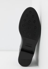 Semelle d'une chaussure habillée noire polie avec des motifs de bande de roulement circulaires et une petite étiquette de marque rectangulaire dans un coin blanc.