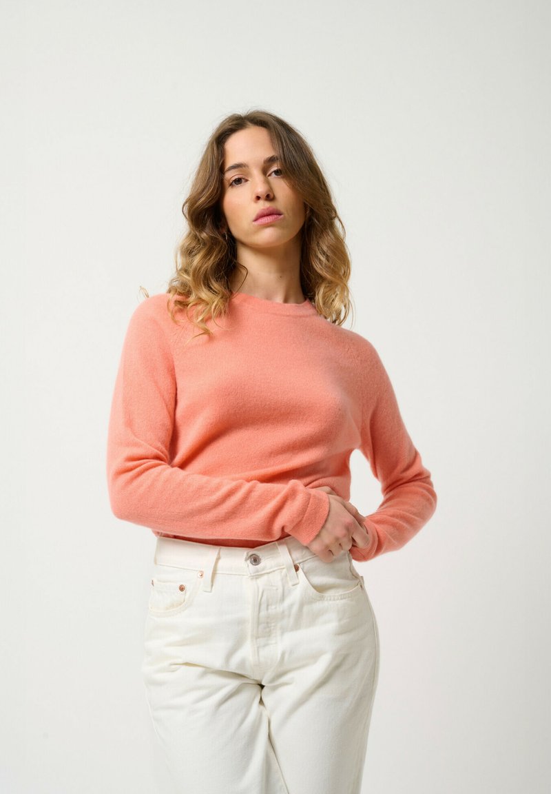 Zachte roze kasjmieren trui met lange mouwen, ronde halslijn en een aansluitende snit, gecombineerd met witte high-waisted jeans. Glad textuur.