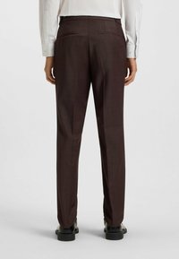Brown tailored trousers with a subtle textured pattern, slim fit, two back pockets, and worn with black shoes.