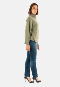 Maglione turtleneck verde chiaro con una vestibilità comoda, polsini a coste, abbinato a jeans skinny blu scuro e scarpe con tacco nere.