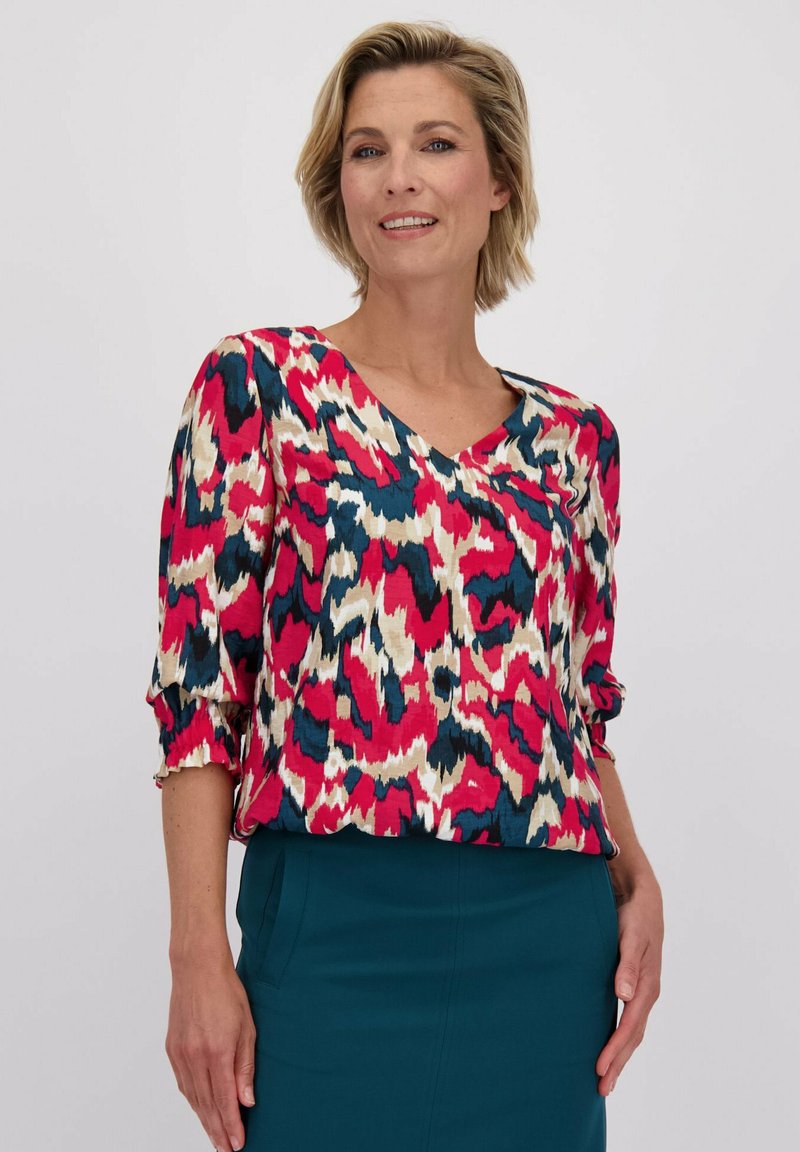 Kleurrijke, patroon blouse met een V-hals en driekwart mouwen. Gemaakt van een lichte stof in tinten van roze, blauw en crème.