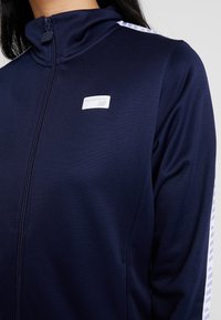 Námořnická bunda na zip s vysokým límcem, texturovanou látkou a kontrastními pruhovanými akcenty na rukávech. Logo na prsou.