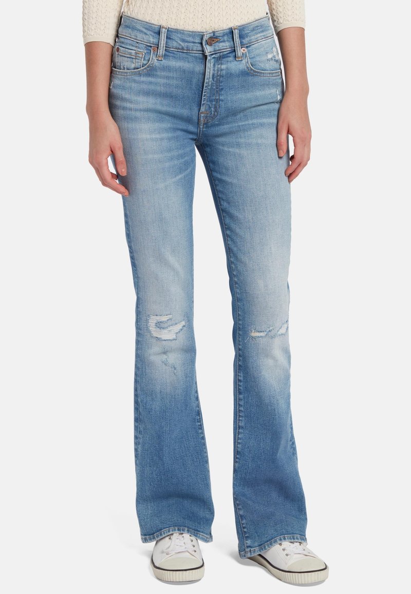 Jeans a zampa d'elefante in denim blu con lavaggio medio, con dettagli strappati sulle ginocchia e una texture leggermente sbiadita. Abbinati a sneaker bianche.