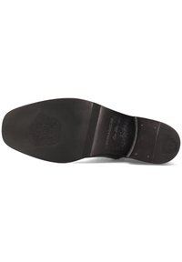 Suela de zapato de cuero negro con un acabado suave, forma ligeramente redondeada, logo en relieve y costuras visibles cerca del talón.