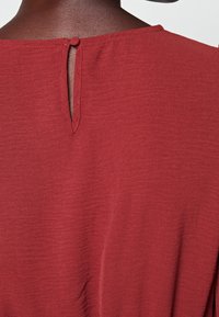 Topp i rustfarve med tekstureret stof, der har en lille nøglehuldetalje bagpå, færdiggjort med rund halsudskæring og glatte kanter.