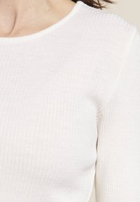 Top bianco a maniche lunghe rigato con scollatura rotonda e texture morbida, dal design aderente che mette in mostra sottili linee verticali.