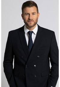 Dubbelzijdig marineblauw colbert met notch-revers, knopen en een borstzak. Gecombineerd met een witte dress shirt en een donkere stropdas.