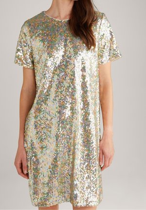 Frau trägt ein kurzärmeliges, knielanges Kleid, das mit mehrfarbigen glänzenden Pailletten bedeckt ist, mit rundem Ausschnitt, steht vor einem einfarbigen Hintergrund.