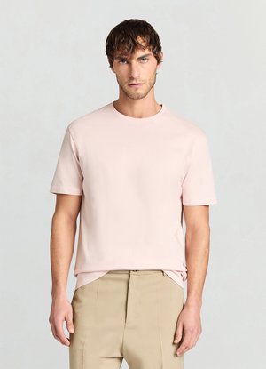 T-shirt rosa chiaro a girocollo in tessuto morbido con maniche corte, abbinata a pantaloni beige. Design semplice, senza motivi o dettagli visibili.