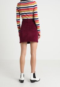Mini falda de pana burdeos con bolsillos traseros, combinada con una blusa de manga larga a rayas multicolores y botas de tobillo en blanco y negro.