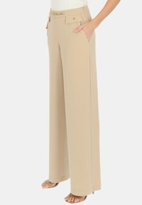 Beżowe spodnie w szerokim kroju wykonane z lekkiego materiału, z dwoma bocznymi kieszeniami, paskiem akcentowanym łańcuchem i gładką fakturą.