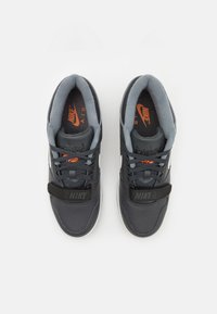 Crne i sive Nike tenisice s teksturiranim gornjim dijelom, podstavljenim ovratnikom i narančastim akcentima na logotipu i ulošku. Čičak remen preko prednje strane.