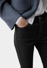 Jean negros de corte ajustado con detalles de costura notables, combinados con una chaqueta de lana gris de textura suave y puños redondeados.