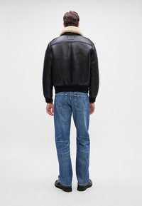 Black leather jacket with a shearling collar, ribbed cuffs, and hem, paired with blue jeans and black shoes. Back view shows design details.