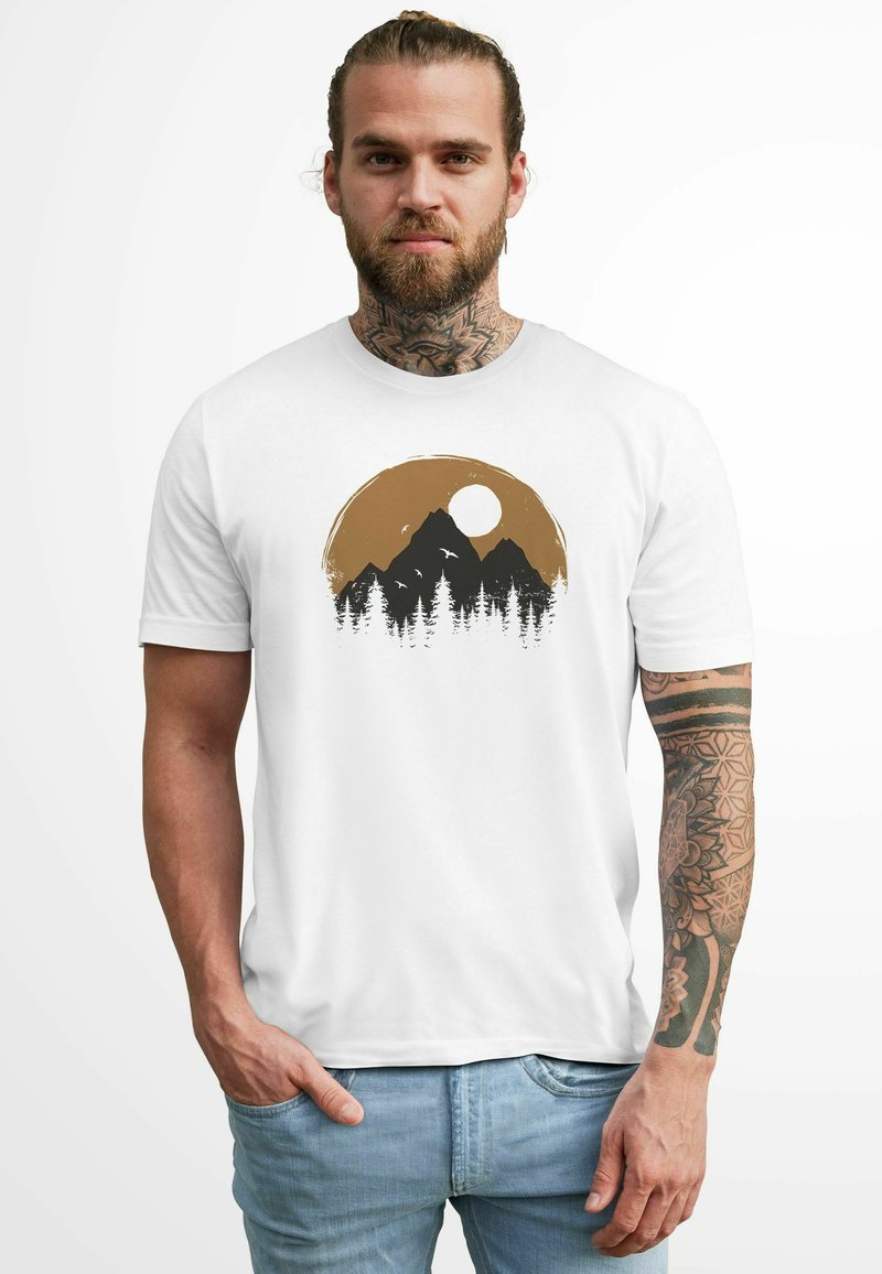 White t-shirt featuring a mountain and forest graphic in black and brown, with a sun design above. Cotton material with short sleeves.