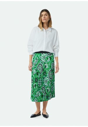 White button-up shirt, green floral pleated skirt with black accents, and black flat shoes. The skirt features a bold, intricate pattern.