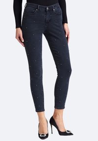 Jeans ajustados de mezclilla oscura con pequeños adornos plateados, que cuentan con una cintura de altura media y un diseño clásico de cinco bolsillos.