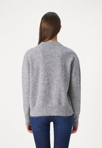 Lys grå ullgenser med rund hals, ribbestrikket nederkant og lange ermer, kombinert med mørkeblå tettsittende jeans.
