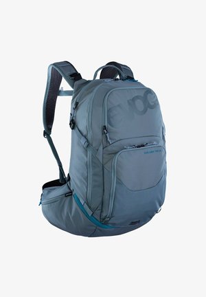 Mochila gris con correas ajustables, acolchado de malla y múltiples compartimentos. Presenta un logo destacado y acentos en color teal contrastante.